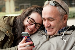 Father and teenage daughter with head in his shoulder sharing something funny in a mobile phone